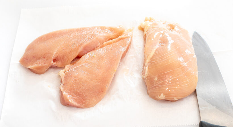 Raw chicken on a cutting board with a chef's knife.