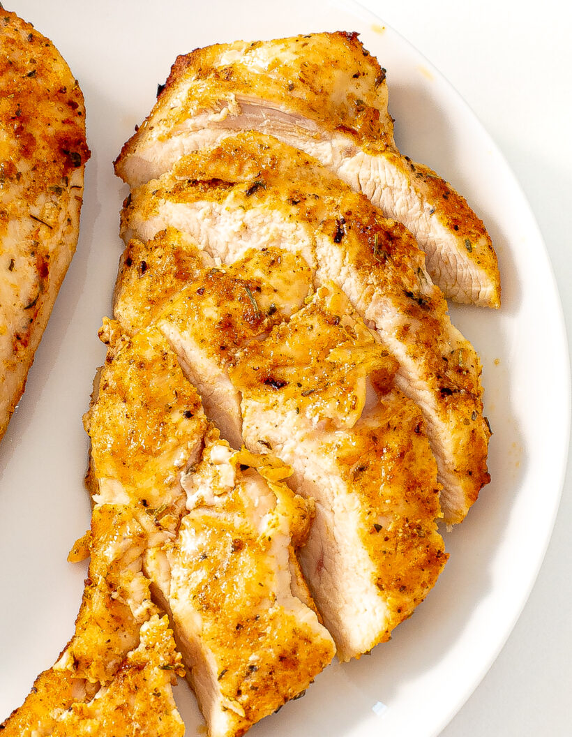 Sliced chicken breast on a white plate with more chicken next to it.