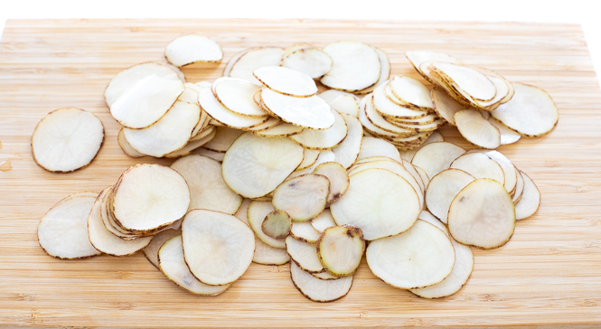 Raw potatoes sliced thinly on a wooden cutting board.