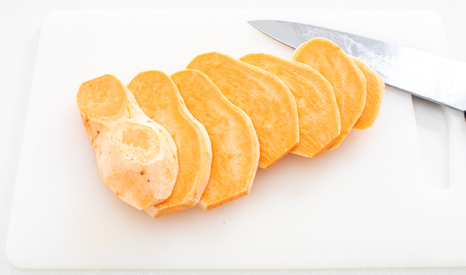 Sweet potato sliced into thin pieces on a cutting board.