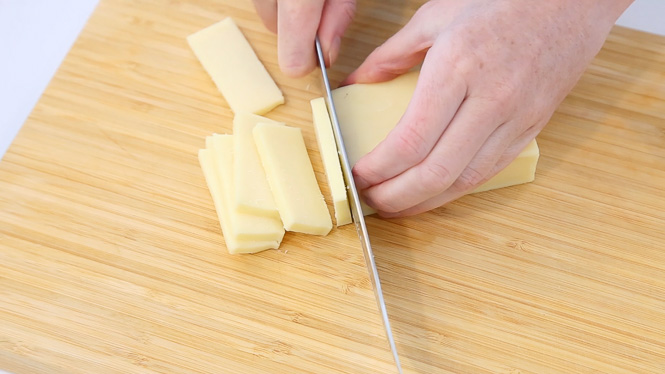 slicing low moisture mozzarella cheese on a wooden cutting board
