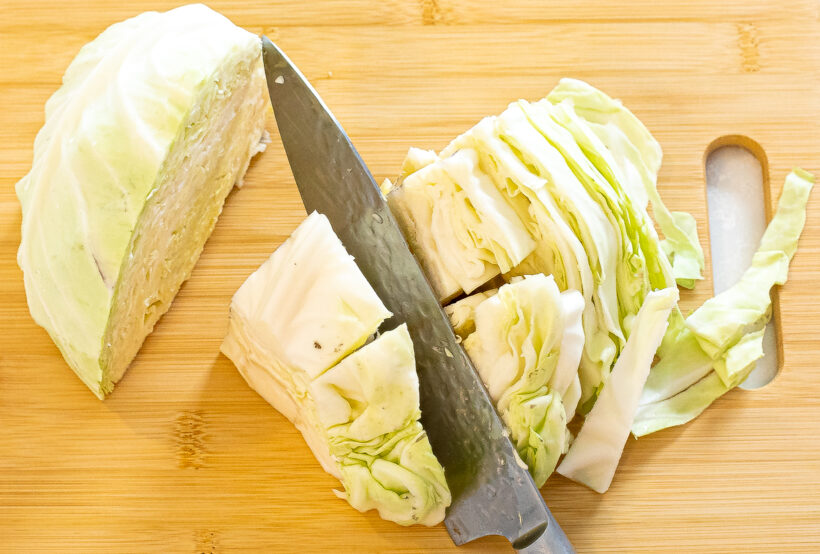 A head of cabbage being chopped on a wooden cutting board. 