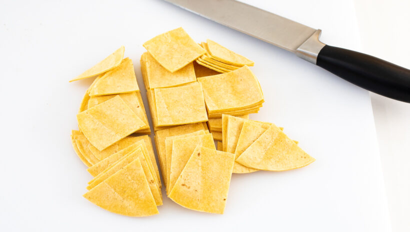 Yellow corn tortillas chopped into squares on a cutting board. 