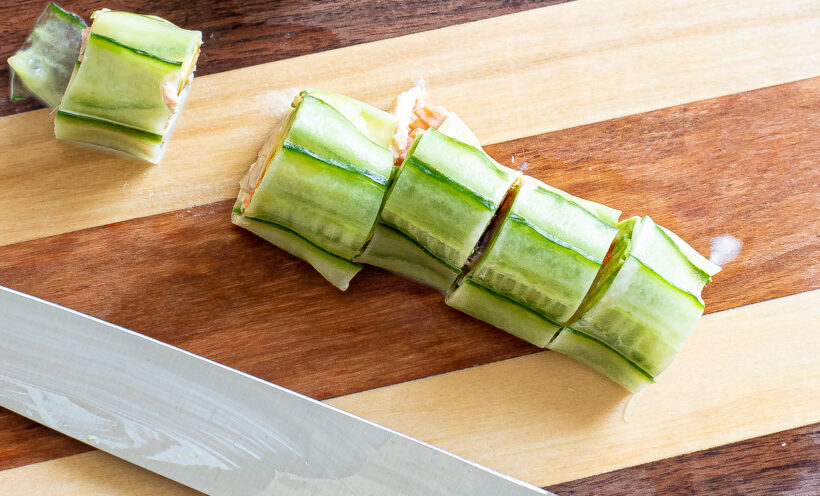 Cucumber sushi roll cut into pieces on a wooden cutting board.