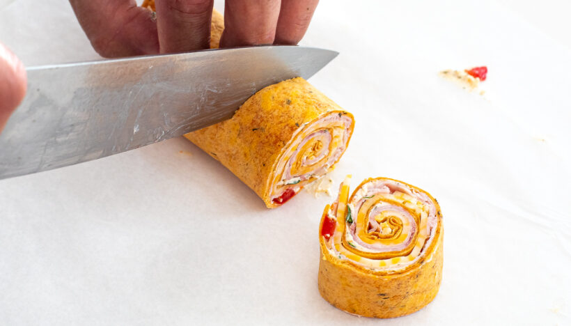 Knife cutting ham and cheese pinwheels.
