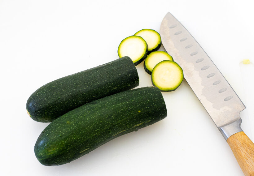 Zucchinis being sliced on a cutting board.