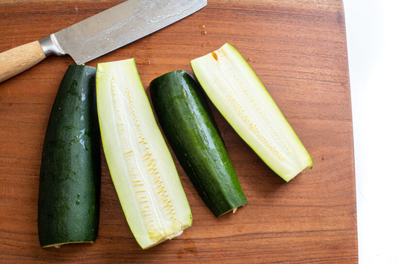 Two zucchinis chopped in half on a wooden cutting board.