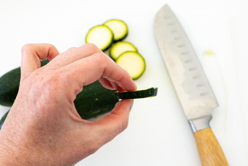 Hand holding up a slice of zucchini to show the thickness.