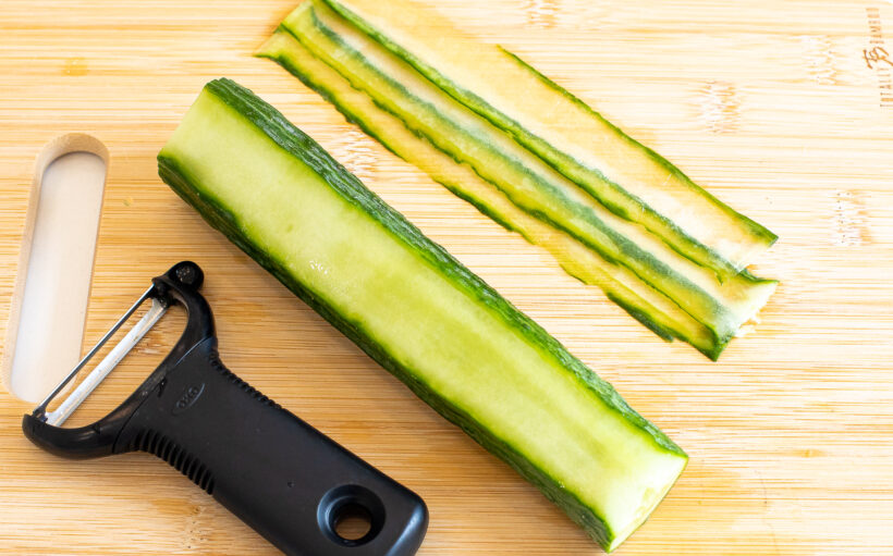Cucumber being sliced into thin pieces with a potato peeler.