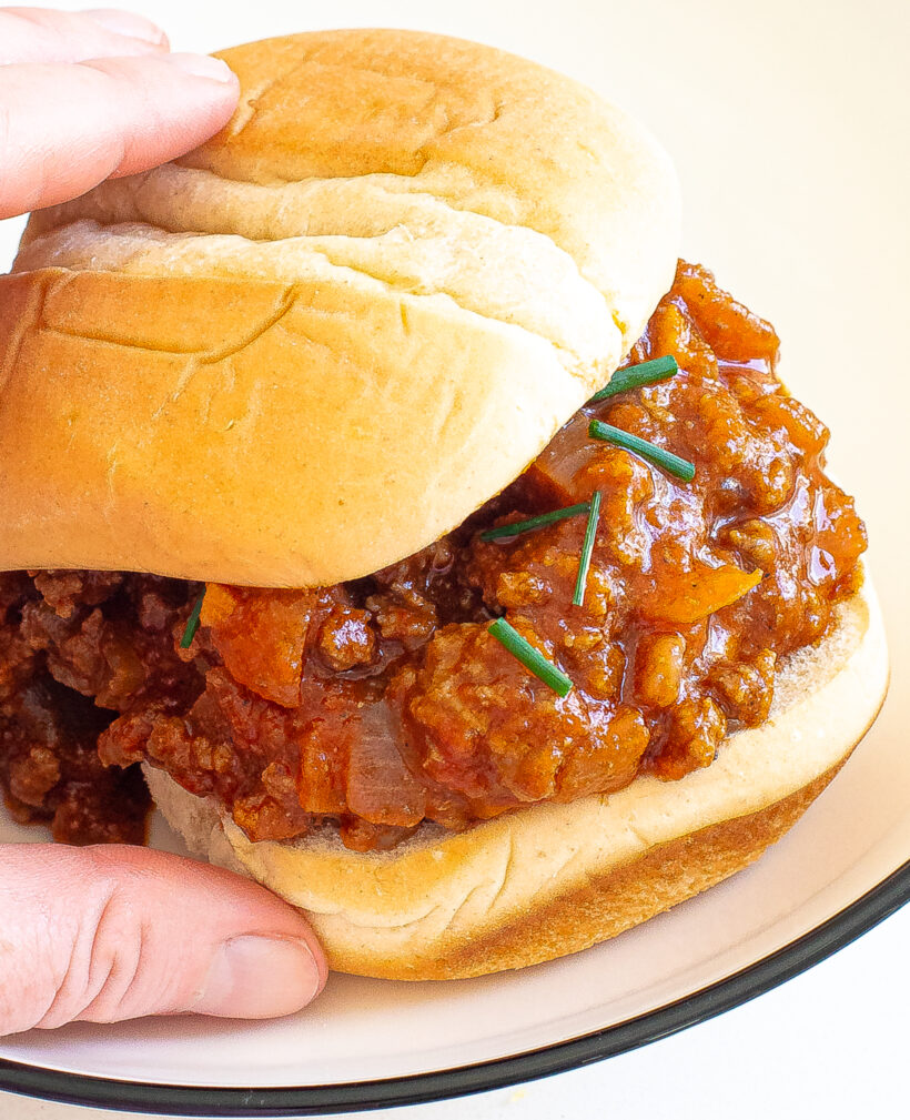 Hand holding a sloppy joe served on a white plate. 