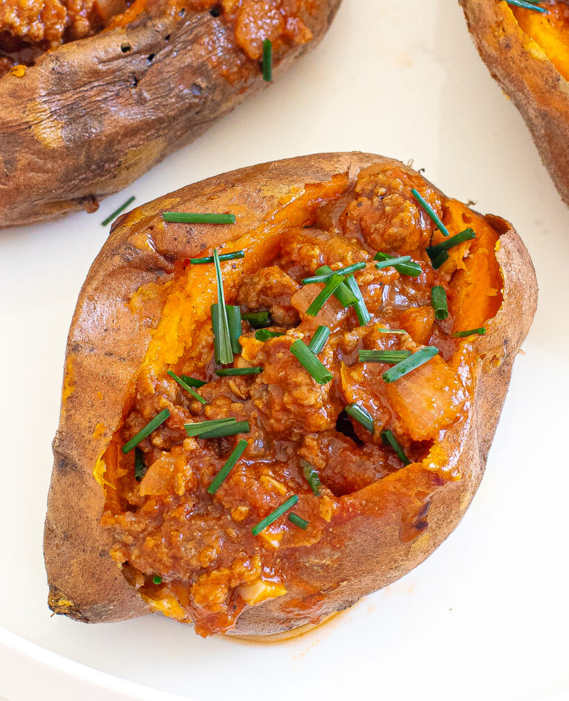 Sloppy joe stuffed sweet potatoes served on a plate topped with chives. 