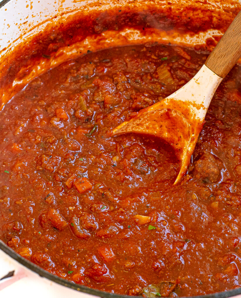 Close up shot of bolognese sauce in a pot with a rubber spoon.