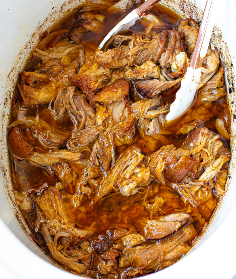 slow cooker pulled pork in crockpot with white tongs