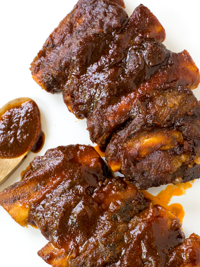 Best Slow Cooker Barbecue Ribs | chefsavvy.com Slow cooker BBQ ribs on a white plate with a wooden spoon coated in barbecue sauce next to them.