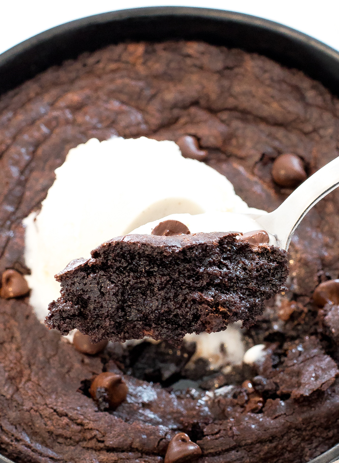 skillet brownies in cast-iron skillet with serving spoon lifting brownie, and ice cream on top