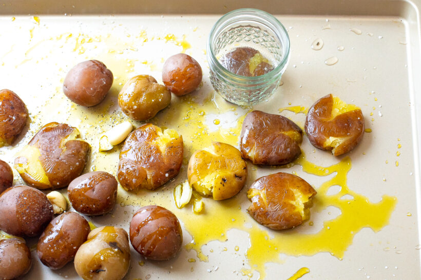 Small jar smashing the potatoes on a baking sheet before baking them.