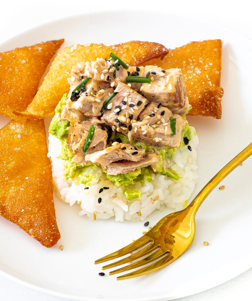 Ahi tuna sushi stack served on a plate with wonton chips and a fork.