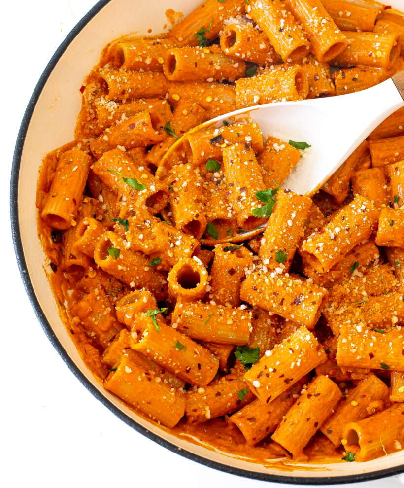 Pasta coated in a creamy red sauce in a skillet with a white spoon. 