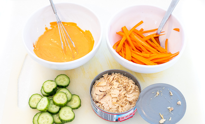Components of a spicy tuna bowl: spicy mayo, carrots, cucumbers, and tuna.