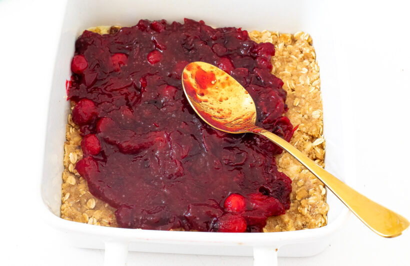 A gold spoon spreading cranberry sauce on top of the crumb crust.