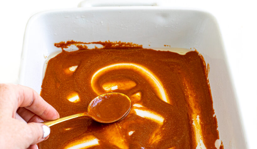 Spoon spreading enchilada sauce into bottom of pan.