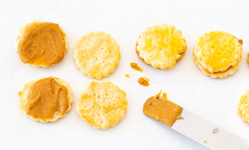 A knife spreading peanut butter on Ritz crackers to make mini cracker sandwiches.