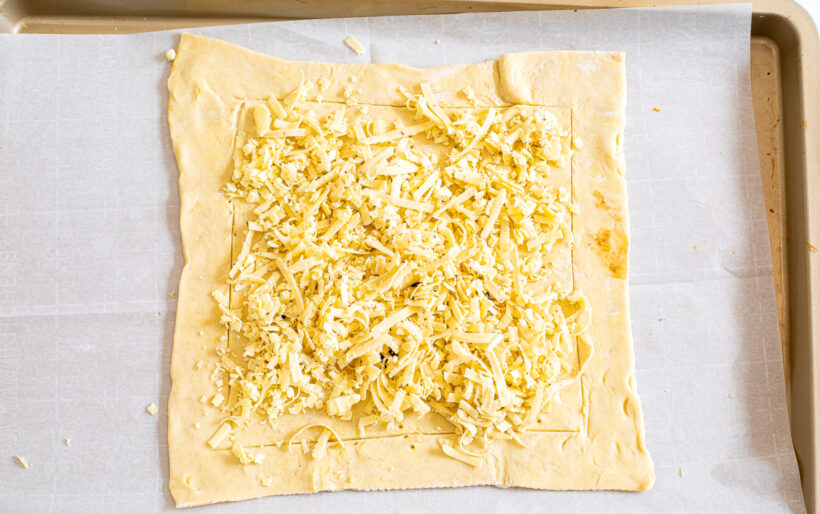Puff pastry on a sheet pan with a layer of shredded cheese on top. 