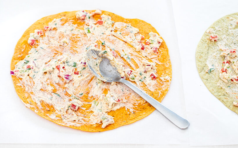 Veggie cream cheese being spread on a large tortilla.