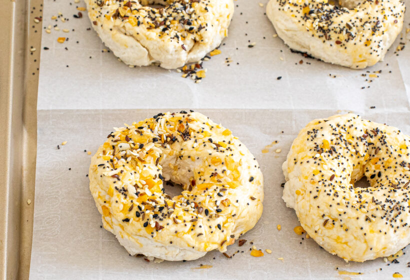 Bagel dough on a baking sheet with everything bagel seasoning on top before being baked. 
