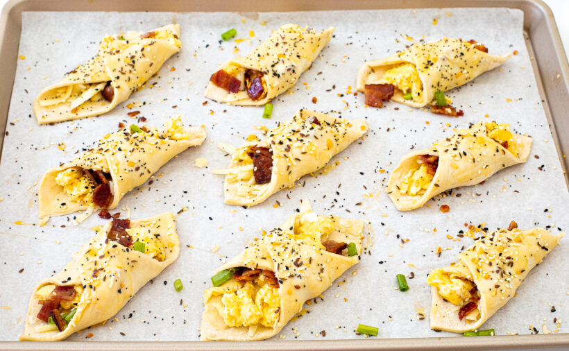 Folded puff pastry squares topped with seasoning and egg wash laid out on a baking sheet lined with parchment paper.