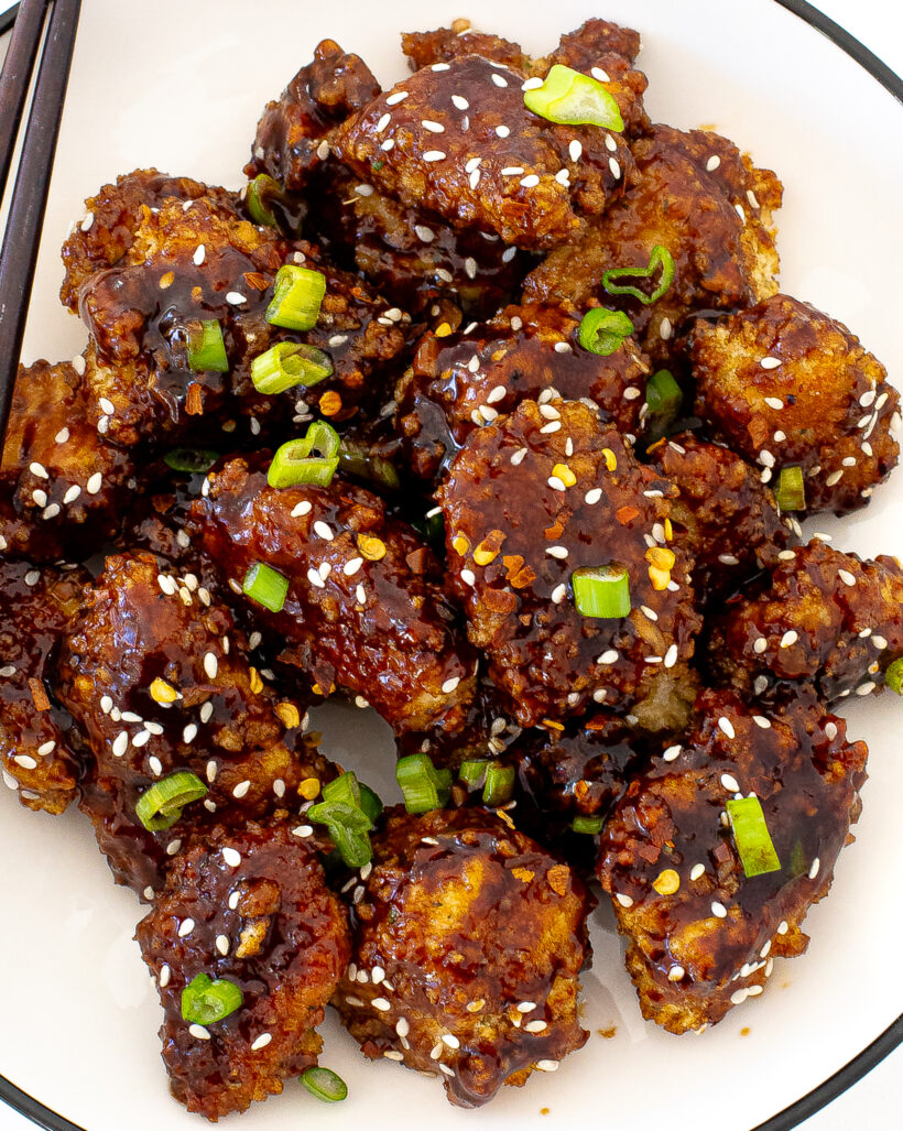 honey sriracha chicken pieces on white plate with green onions and sesame seeds