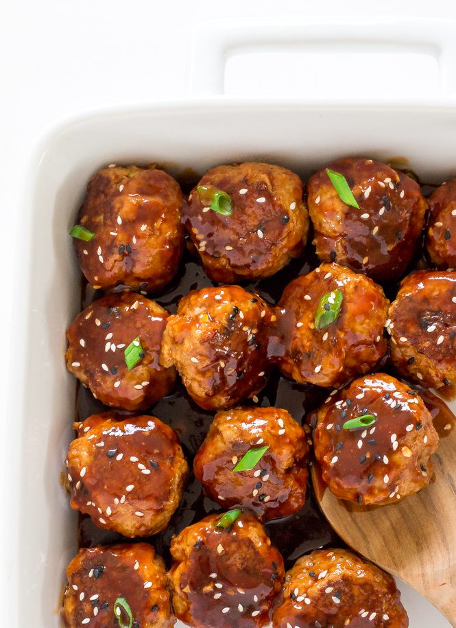 slow cooker sriracha meatballs in a white baking dish garnished with scallions and sesame seeds