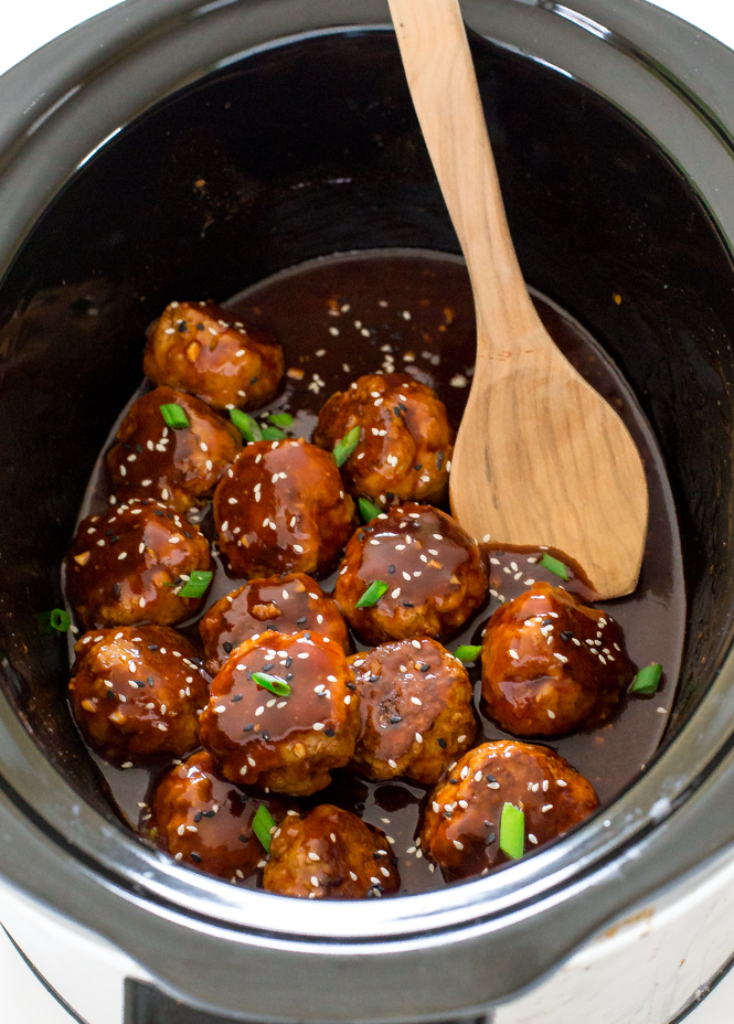 slow cooker sriracha meatballs inside a crock pot with a wooden spoon
