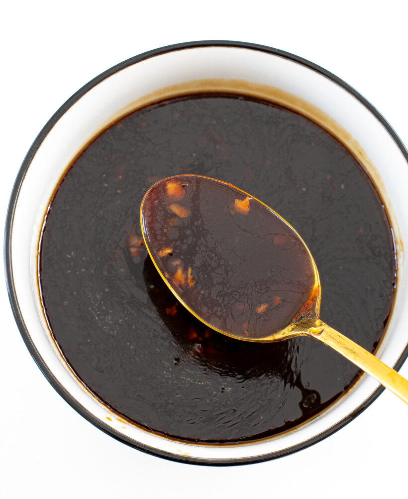 A top down view of a bowl of stir fry sauce with a gold spoon holding a spoonful above it.