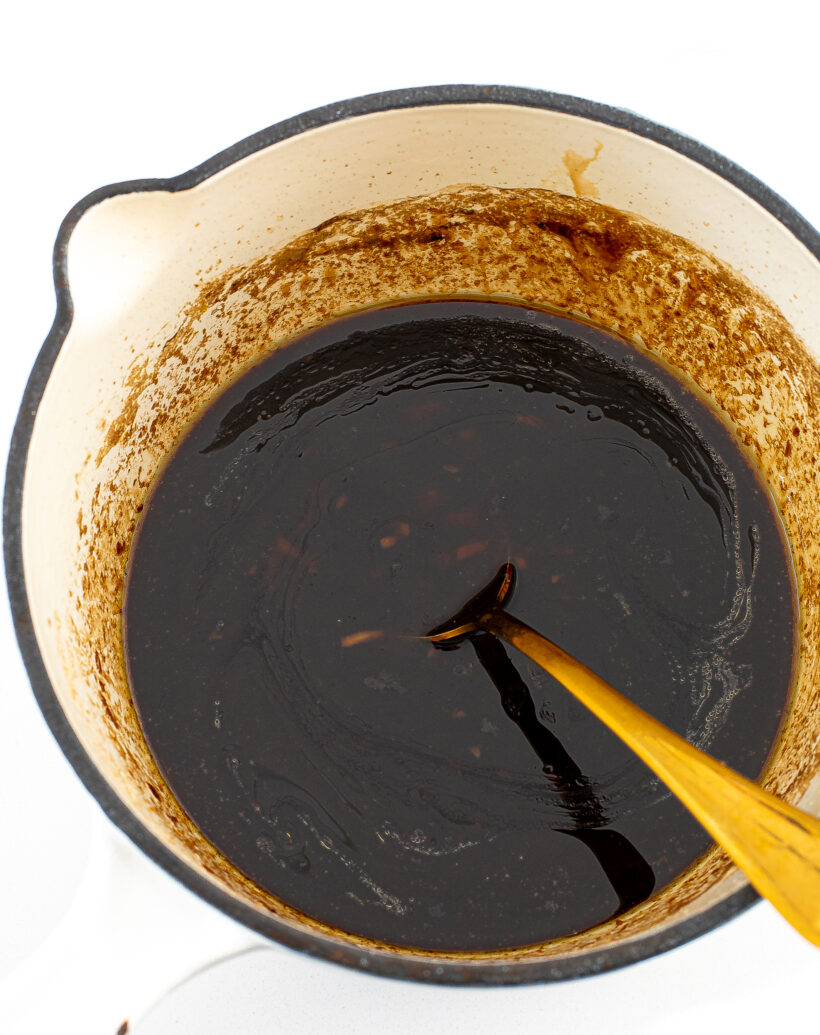A top down view of stir fry sauce in a saucepan stirred with a gold spoon.