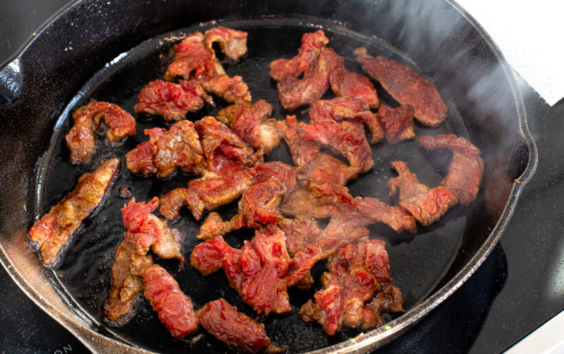 Sliced flank steak in a skillet with oil.