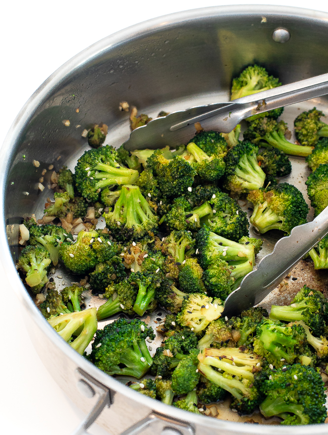 Broccoli in a silver sauté pan with silver tongs in the pan. 