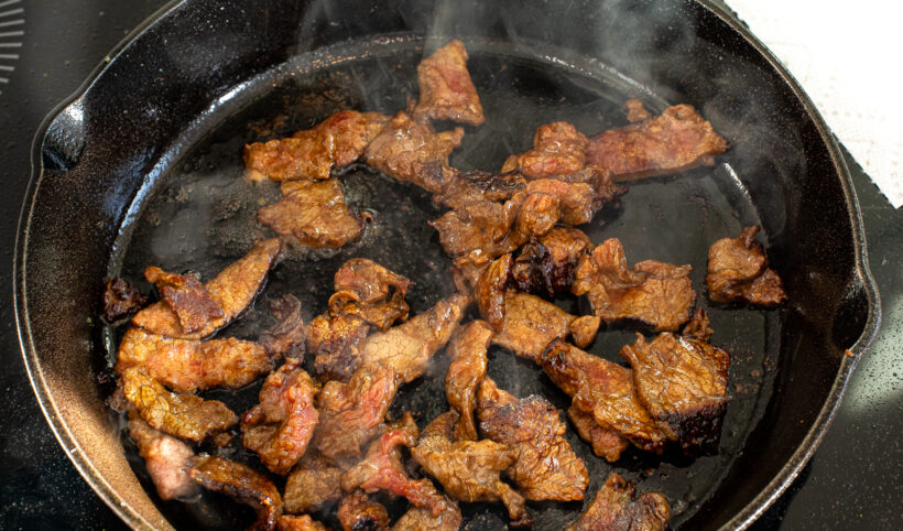 Cooked flank steak in a skillet with oil.