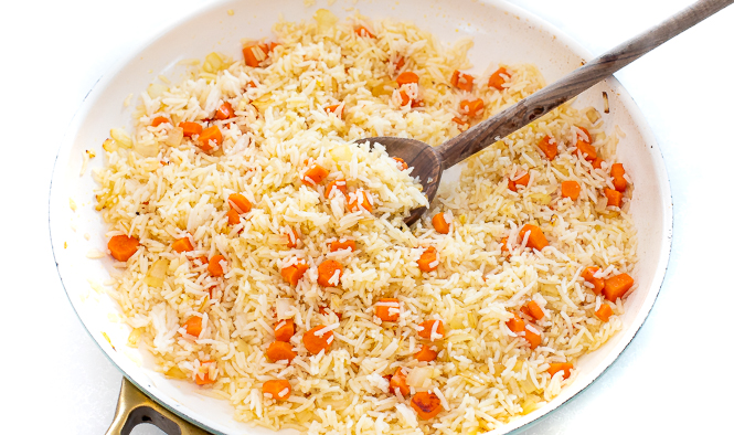 White rice, carrots and onions in a white skillet with a wooden spoon.