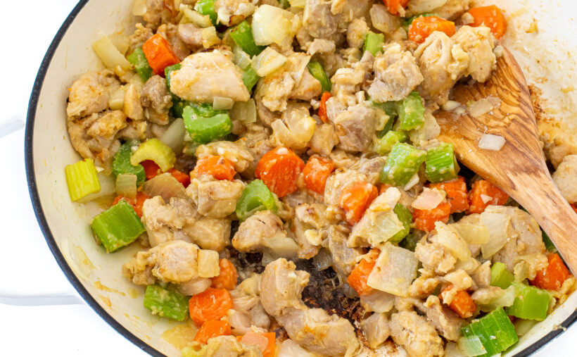 The stew mixture in a white skillet with a wooden spoon stirring it.