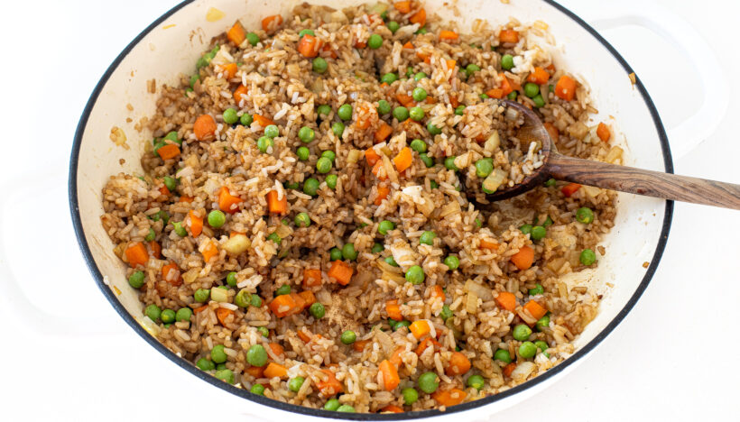 Vegetables and rice in a skillet with a wooden spoon.