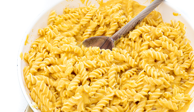 Noodles in cheese sauce in a white pan with a wooden spoon.