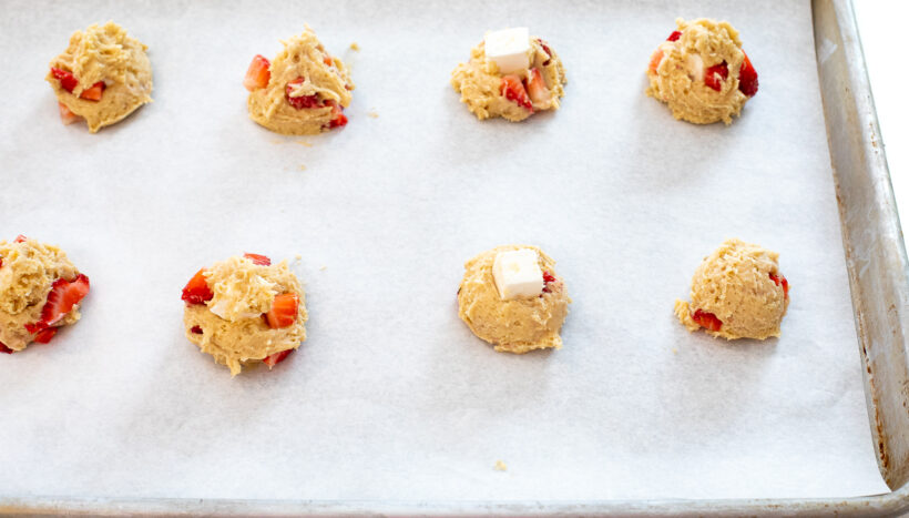 Cookie dough balls lined up on a baking sheet lined with parchment paper.