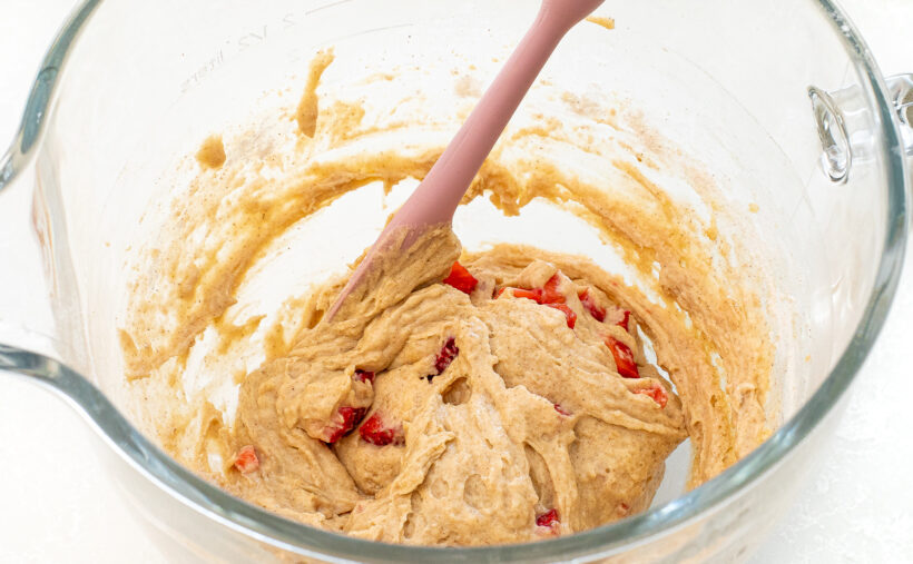 Mixing bowl with cake batter and pieces of strawberry being mixed together. 