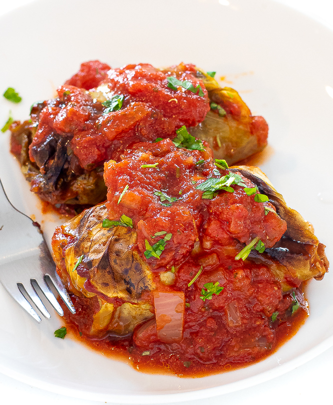 Two cabbage rolls on a white plate smothered in tomato sauce. 