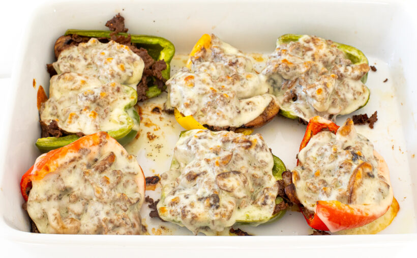 Melted cheese on top of stuffed bell peppers in a white baking pan.