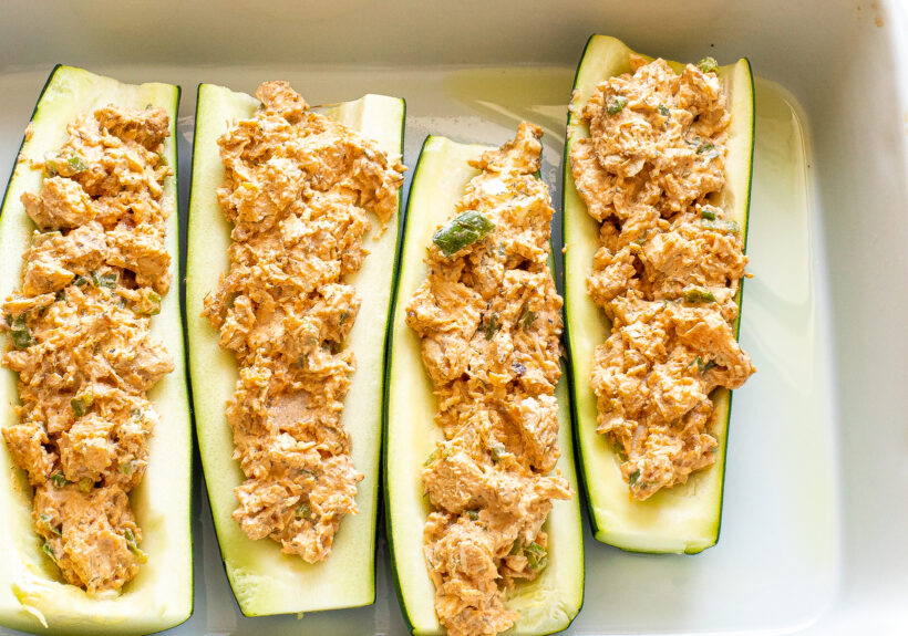 Zucchini boats filled with buffalo chicken mixture in a baking dish.