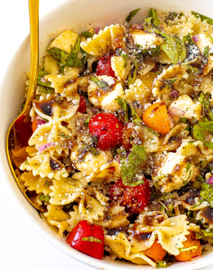 Overhead shot of bruschetta pasta salad in a serving bowl with a golden spoon. 