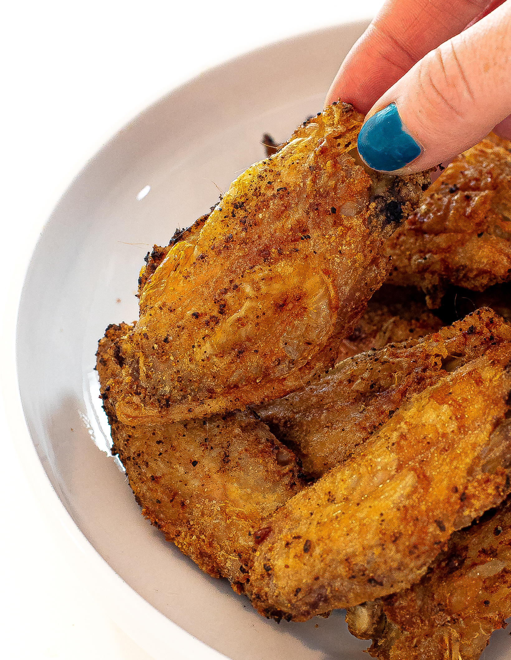 Hand picking up a chicken wing from the pile on a plate.