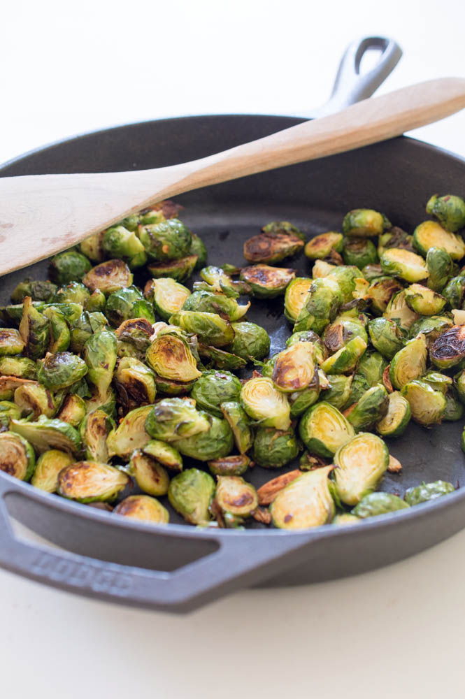 Brussels sprouts in a cast iron pan with a wooden spoon on top. 